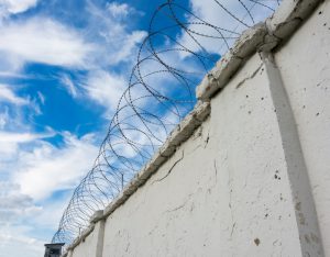 Prison wall with barbed wire and a watchtower on blue sky background