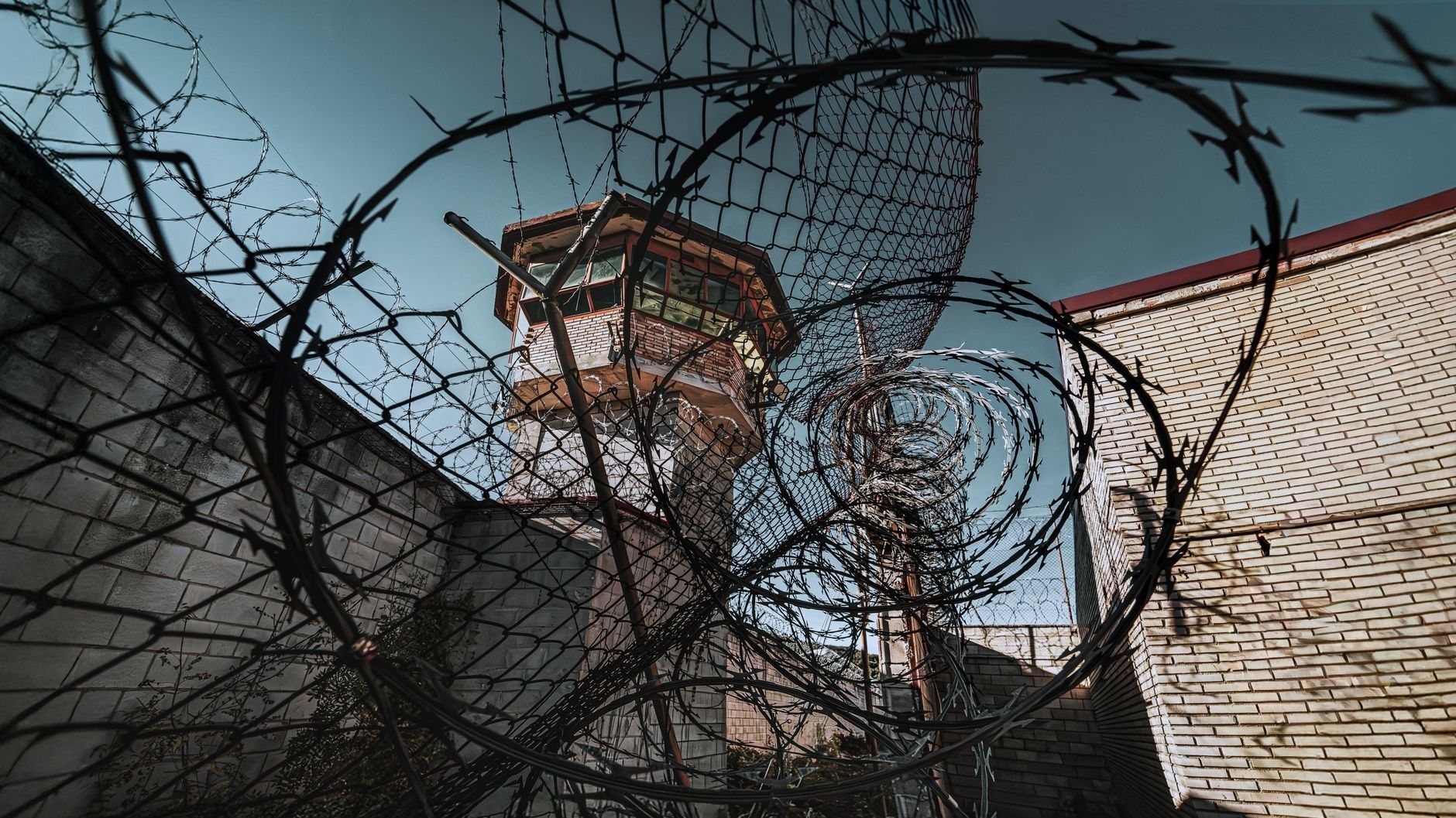 Gefängnishof mit Wachturm und dichtem Stacheldraht vor blauem Himmel